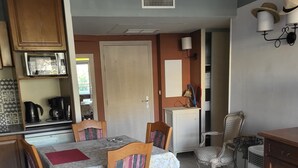 A dining area with a table set for four, surrounded by wooden chairs, a white cabinet, and a small refrigerator. - NICE ANTIBES SAINT LT CANNES RIVIERA BEACH POOL TENNIS SOLARIUM PARKING CAMERAS (Cagnes-Sur-Mer)