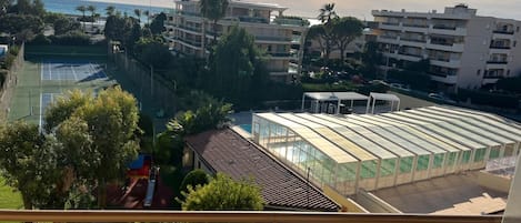 A residential area with a tennis court, a greenhouse, and apartment buildings.
