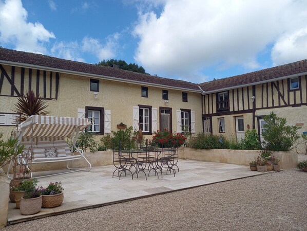 Une cour avec une table et des chaises, entourée de plantes en pot et d’une chaise à rayures.