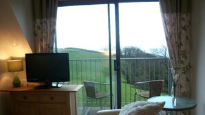 A room with a television on a wooden cabinet, a small table with a vase, two chairs, and a balcony with a view of a green landscape. - Your Sea View Studio with Balcony and Terrace - WIFI (strete)