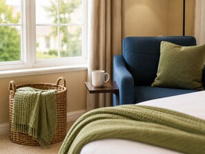 A room with a bed, a blue armchair, a white mug, a green throw, and a wicker basket.
