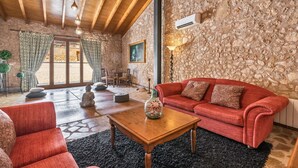 A cozy living room with a stone wall, wooden ceiling beams, a red sofa, a coffee table, and a stone statue. - Son Monserrat, fantastic for two families. (Petra)