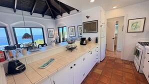 A kitchen with a large island, white cabinets, and a view to the outside. - Caribbean Cottage with Breathtaking Views and Your Own Private Pool! (Cruz Bay)