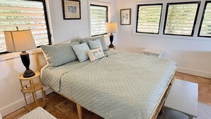 A bedroom with a bed, bedside tables, lamps, and a view through the windows. - Caribbean Cottage with Breathtaking Views and Your Own Private Pool! (Cruz Bay)
