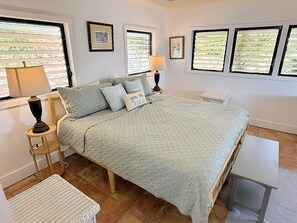 Un dormitorio con cama, mesitas de noche, lámparas y vistas a través de las ventanas.