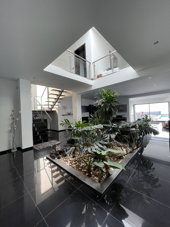 A modern interior with a central indoor garden, a staircase, and a mezzanine level.