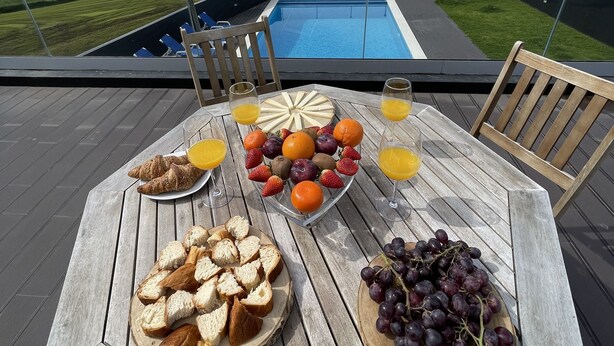 Ein Tisch mit Speisen und Getränken auf einer Terrasse mit Blick auf einen Pool und das Meer.