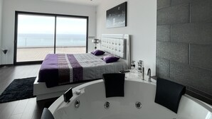 Ein modernes Schlafzimmer mit einem großen Bett, einer Badewanne und Blick auf den Ozean.