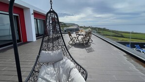 Ein moderner Außenbereich zum Sitzen mit einer Hängematte, einem Tisch mit Obstkorb und Blick aufs Meer.