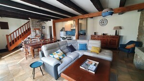 Sala de estar con sofá, mesa de centro y comedor con sillas y una mesa. Se ve una cocina al fondo.