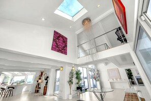 A spacious interior with a high ceiling, a skylight, a dining area, and a staircase leading to an upper level. - Beverly Hills Dream Home with pool and view hidden down private celebrity lane. (Beverly Hills)