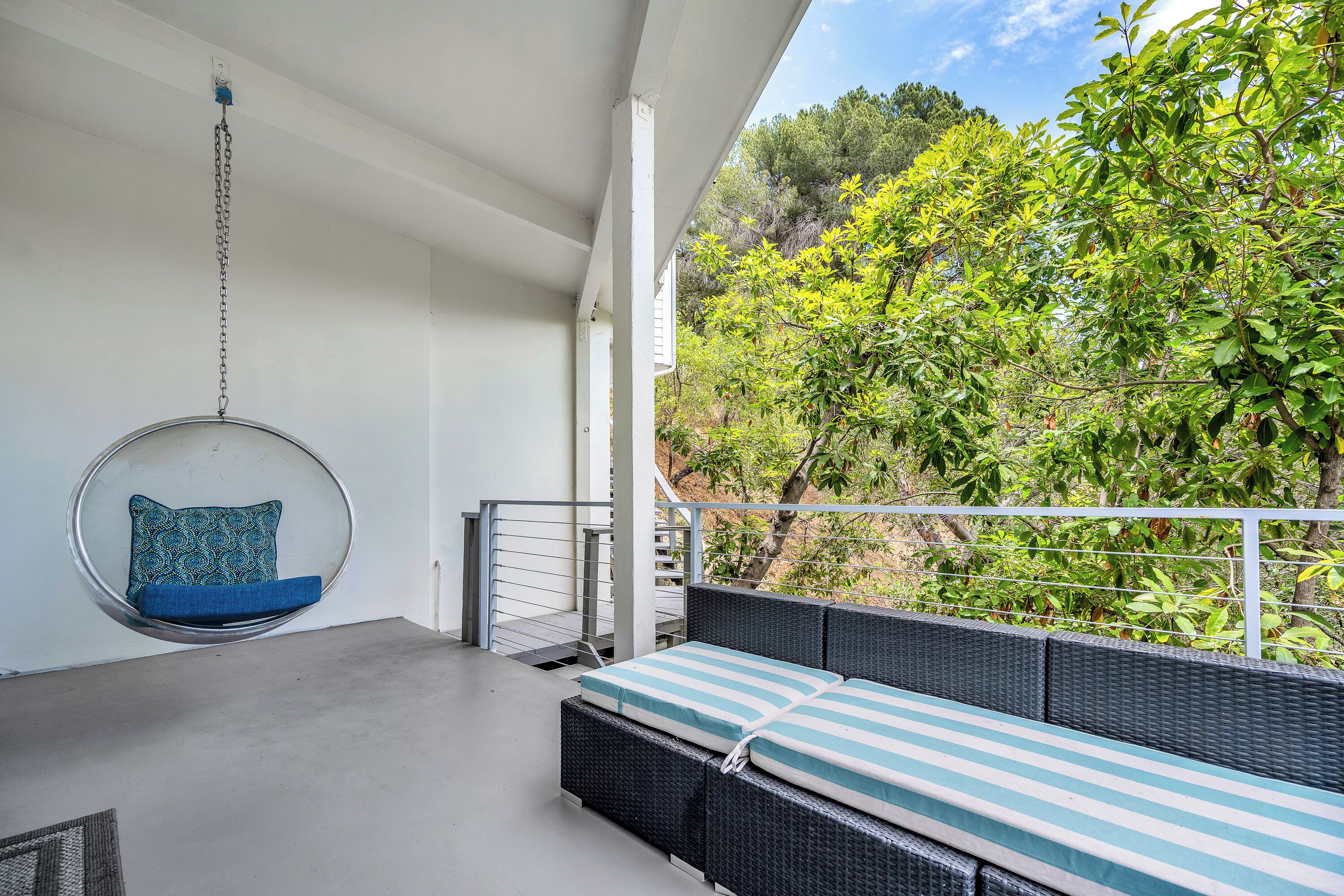 Ein Balkon mit einer Hängematte, einer gepolsterten Bank und Blick auf Grünflächen.