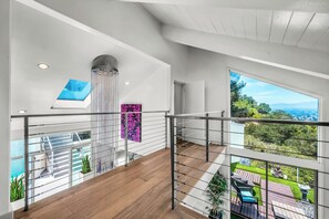 A spacious balcony with a view of greenery and distant mountains, a modern interior with a high ceiling, and a decorative column.