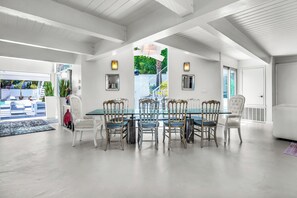 A modern dining area with a glass table surrounded by chairs, a view of the outdoors, and a staircase leading to a balcony.
