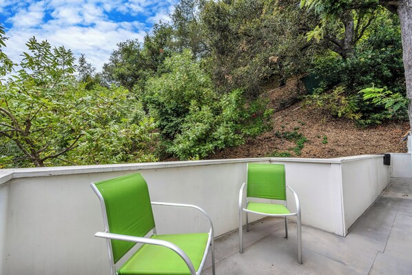 A terrace with two green chairs and a white wall.