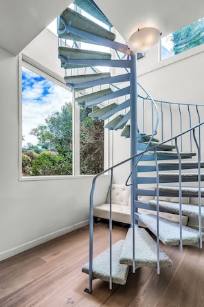 A spiral staircase with a light fixture at the top, leading to a room with a large window and a white sofa. - Beverly Hills Dream Home with pool and view hidden down private celebrity lane. (Beverly Hills)