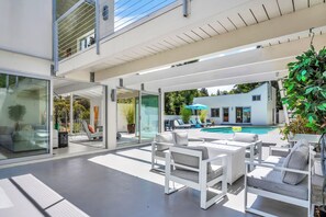 Un espace de vie extérieur moderne doté d’une piscine, d’un coin salon et de portes vitrées donnant sur un jardin.