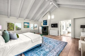Une chambre à coucher avec un lit, une télévision, une cheminée et une salle de bain visible à travers une porte ouverte.