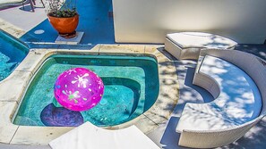 A swimming pool with a pink ball, a potted plant, and wicker furniture.