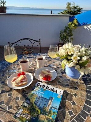 Une table dressée avec de la nourriture, des boissons et un magazine, sur une terrasse offrant une vue panoramique.