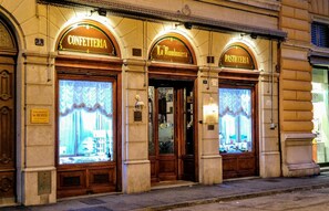 Un bâtiment comprenant trois devantures de magasins portant les inscriptions « CONFETTERIA », « La Bomboniera » et « PASTICCERA ».
