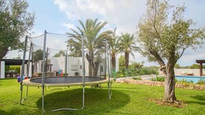 Un trampolino in un prato verdeggiante con una piscina e palme sullo sfondo.