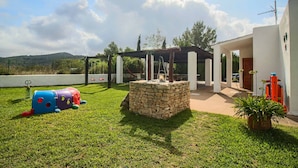 Spazio esterno curato con una struttura in pietra, una zona relax coperta e un'attrezzatura da gioco colorata per bambini.