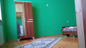 A room with a wooden floor, a large mirror, a wardrobe, a bed with a patterned bedspread, and a green wall. - About house......... (Quba)