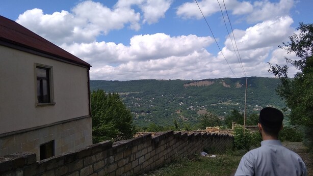 A building with a red roof and a window, overlooking a valley with houses and greenery. - About house......... (Quba)