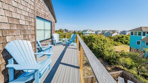 A wooden deck with blue Adirondack chairs and a view of houses in the background. - Turtle Shack - Duck, Sea Tern, Oceanside, Beach 150 Yds, Pool, Pets OK, Flex Stays (Duck)