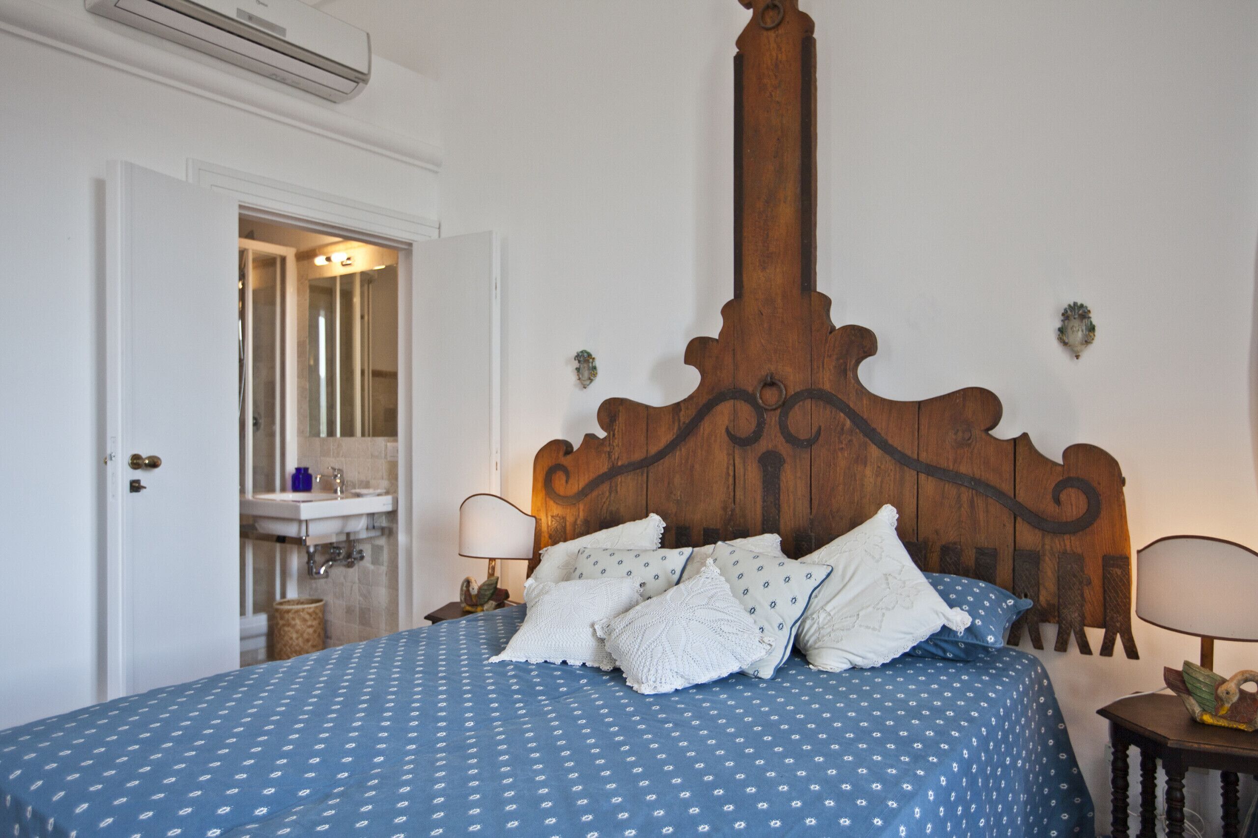A bedroom with a wooden headboard, a blue bedspread, and two bedside lamps.