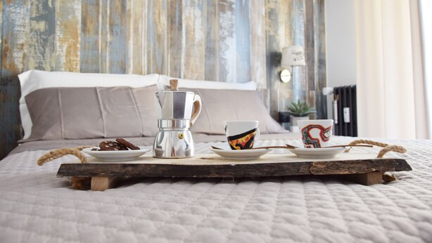 Een bed met een houten dienblad waarop een koffiezetapparaat, een kop en een bord met eten staan.