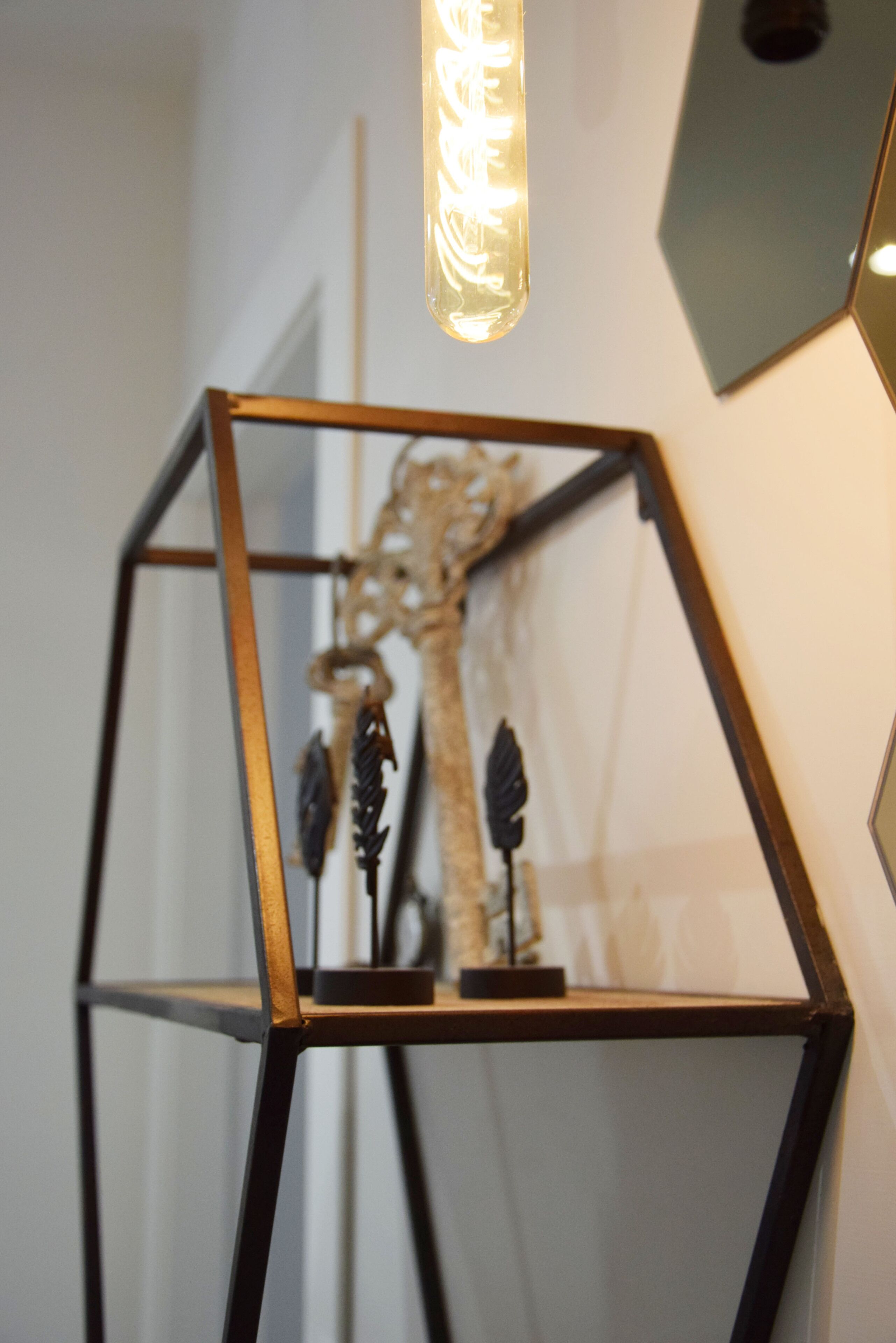 A geometric metal frame structure with a hanging light fixture and a decorative item inside.
