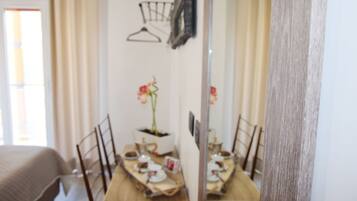 A dining area with a table set for two, a potted plant, and a mirror reflecting the room.