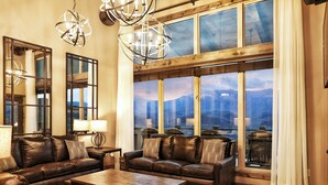 A spacious living room with leather sofas, a wooden coffee table, and large windows offering a view of mountains.