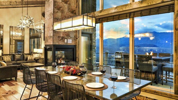 A dining area with a large table, chairs, and a view of mountains through large windows.