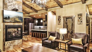 A cozy living room with a fireplace, leather chairs, a wooden dining table, and a kitchen in the background.