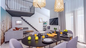 A modern living room with a dining area, featuring a staircase, a flat-screen TV, and a large window with sheer curtains. - Villa Remusic, Pool, whirlpool, Sauna,6 bedrooms, amazing landscape (Smolonje)