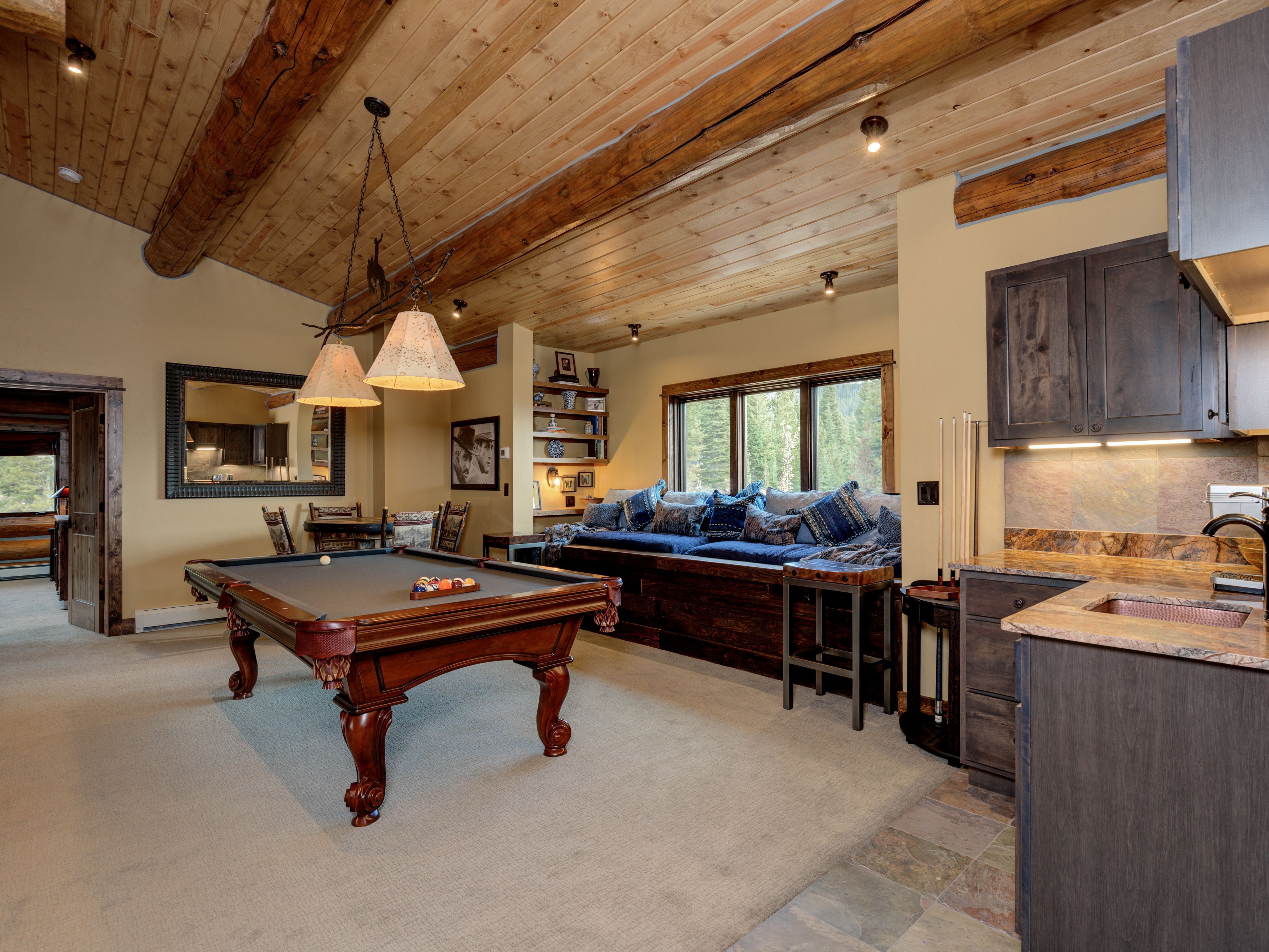 A cozy living room with a pool table, a comfortable seating area, and a kitchen with dark wooden cabinets.