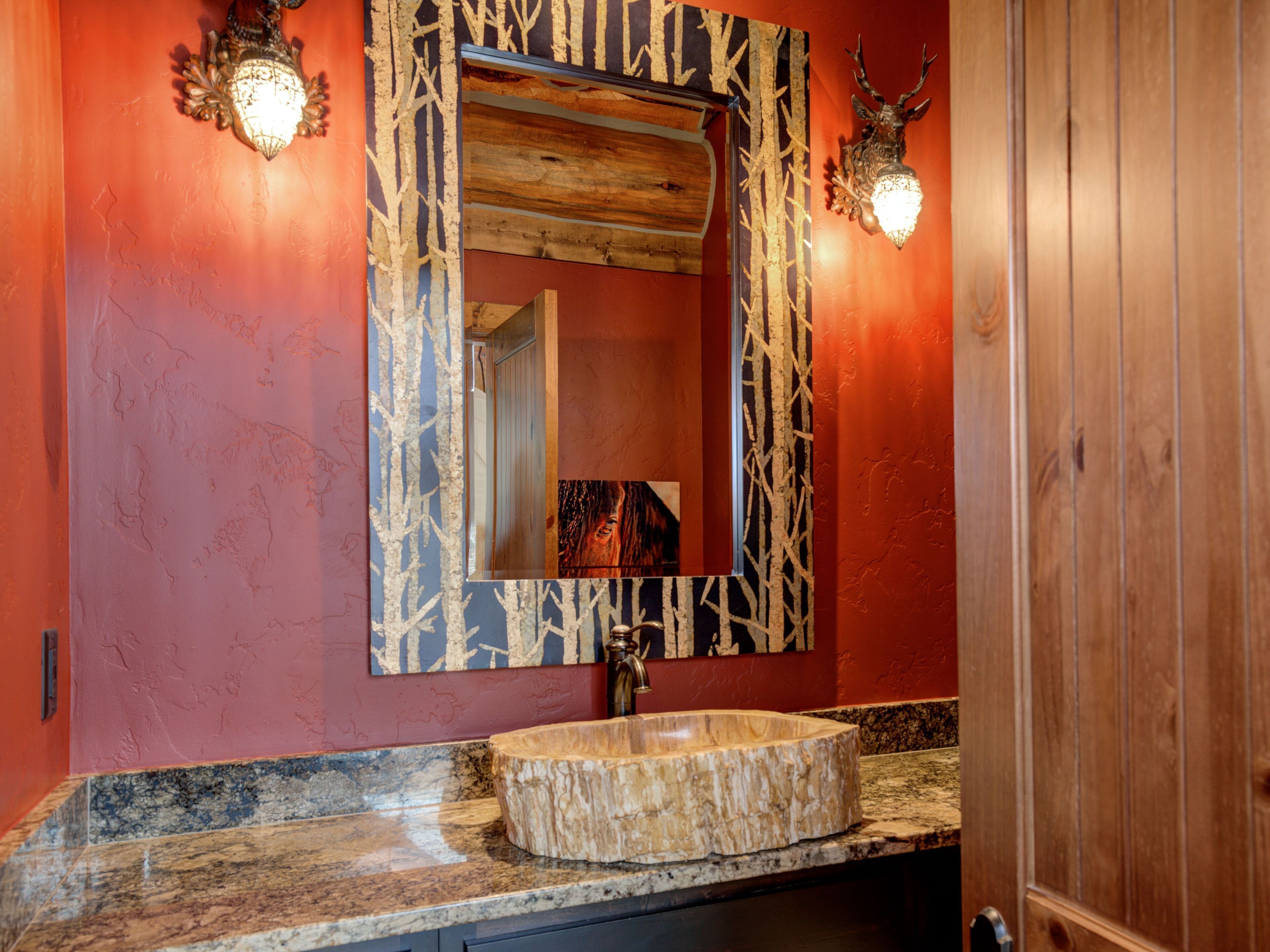 Une salle de bain avec un meuble-lavabo en bois, un lavabo rond en marbre et un miroir orné d’un motif représentant une branche d’arbre.