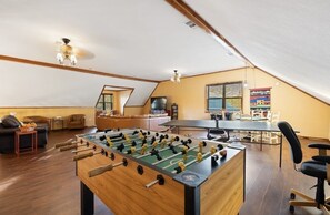 Un salón amplio con mesa de fútbol, sofá, mesa de centro y televisor.
