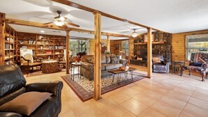 Uma sala de estar ampla com lareira, estantes de madeira, móveis de couro e ventilador de teto.