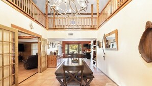 Uma sala de jantar espaçosa com uma longa mesa de madeira e cadeiras, uma escada de madeira e uma luminária rústica no teto.