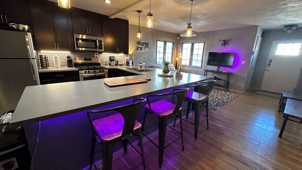 A modern kitchen with dark cabinets, stainless steel appliances, and a bar area with purple lighting. - Private house in a safe area, close to Nob Hill, UNM, Airport, Netflix, and KAFB (Albuquerque)