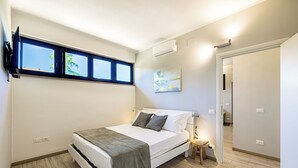 Ein Schlafzimmer mit einem Bett, einem Nachttisch, einem Fenster und einem Bild an der Wand.