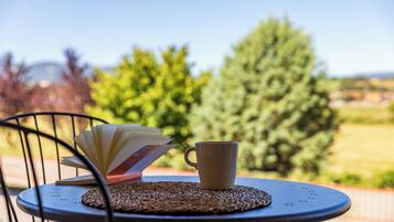 A table with a cup and an open book on a woven placemat, outdoors with trees in the background.