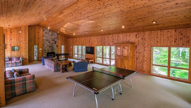 Una habitación amplia con mesa de ping pong, sofás escoceses y chimenea de piedra.