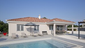 Una casa moderna con piscina, mobiliario de exterior y un patio cubierto.