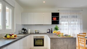 Una cocina moderna con armarios blancos, horno empotrado, cafetera y frutero.