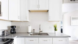 A modern kitchen with white cabinets, a stainless steel sink, a coffee maker, and a toaster. - Stylish 2 Bedroom Camelback (Phoenix)